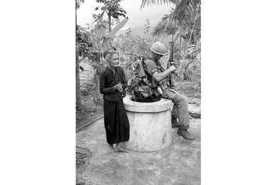 Vietnamese peasant stands before her burning home in Que Son Valley. Vietnamese peasant woman stands next to a sitting 1st Cavalry soldier.