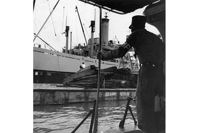 Freighter unloading in the harbor is checked by Army MP patrol, as are barges used to bring cargo ashore.