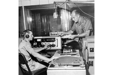 Radio production is discussed in the control room by SP4 Larry Renaud and James Mayall.