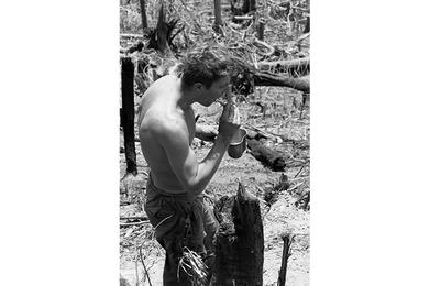An unidentified soldier brushes his teeth, the desolate and torn-up landscape of Hill 937 of Dong Ap Bia, better known to Americans as Hamburger Hill, stretching on behind him.