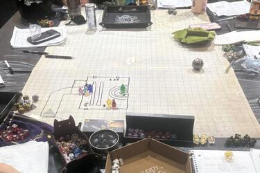 A Dungeons and Dragons playing board sits on a table surrounded by dice, paper and notebooks.
