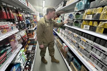 An airman in camouflage uniform looks at energy drinks on a store shelf.