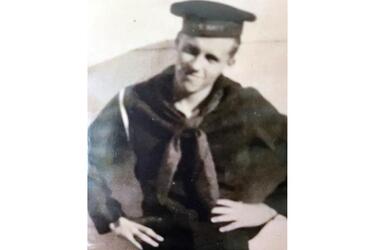 A black-and-white, 1940s-era portrait of a Navy sailor in hat and uniform posing with his hands on his hips.
