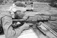 Pfc. Ron Fuller of Indianapolis, Ind., his head bandaged after being hit by shrapnel and his AR-15 at the ready, watches for the enemy from atop an armored personnel carrier.
